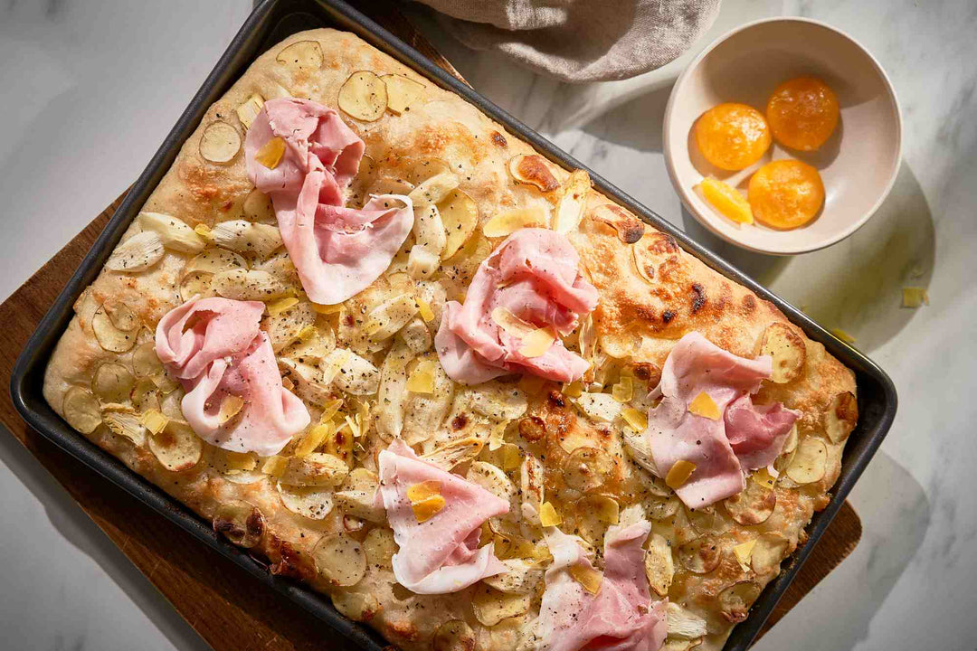 Pizza bianca with white asparagus, sliced potatoes, ham and cured egg next to a bowl with cured egg yolks.