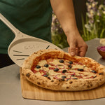 pizza being placed on bamboo pizza peel and serving board with wide turning peel 